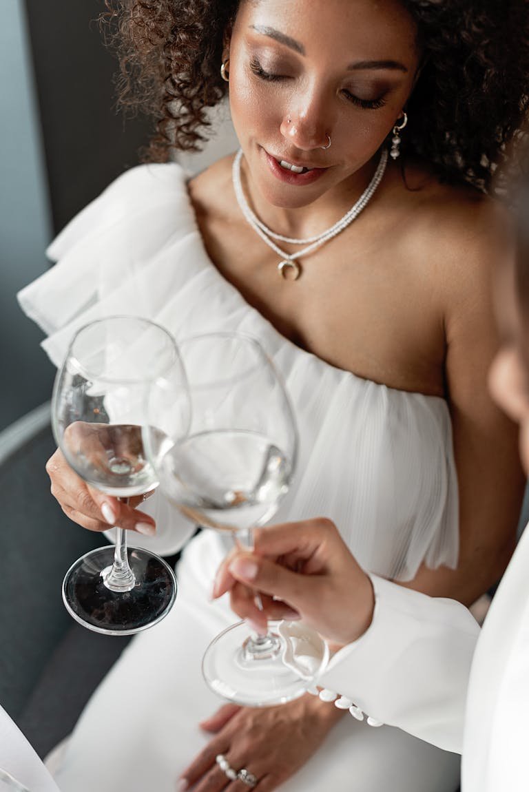 Elegant woman in white dress holding wine glasses in a celebratory toast.