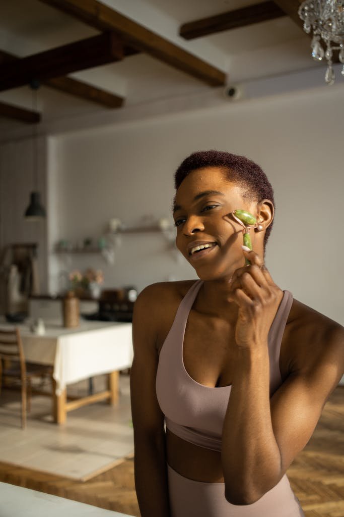 A woman in activewear using a jade roller for her skincare routine in a cozy indoor setting.