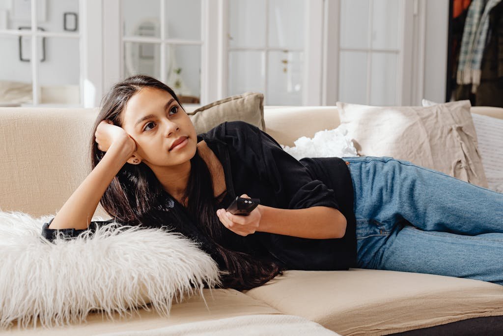 Woman lounging on a sofa with remote in hand, enjoying indoor relaxation.