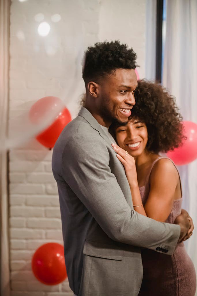 A delighted couple sharing an embrace surrounded by festive balloons in a cozy indoor setting.